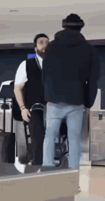 a man in a black jacket is standing next to a man in a white vest and talking to him .