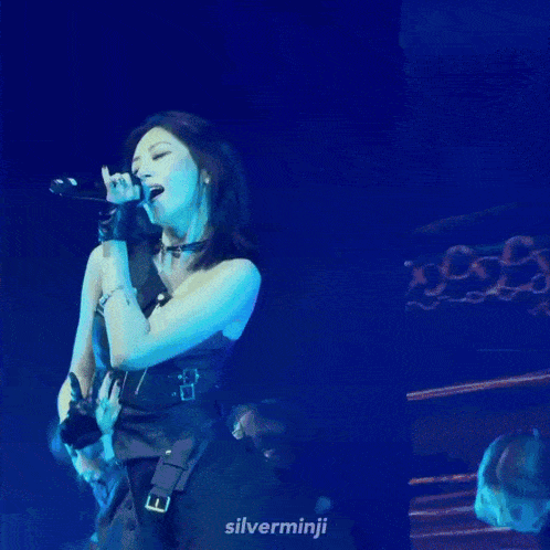 a woman is dancing on a stage in front of a microphone while another woman looks on .