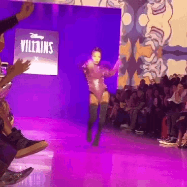 a woman is walking down a runway in front of a screen that says villains