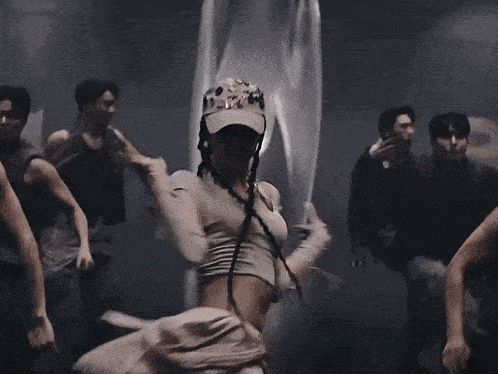 a group of people are dancing in a dark room and one of them is wearing a hat