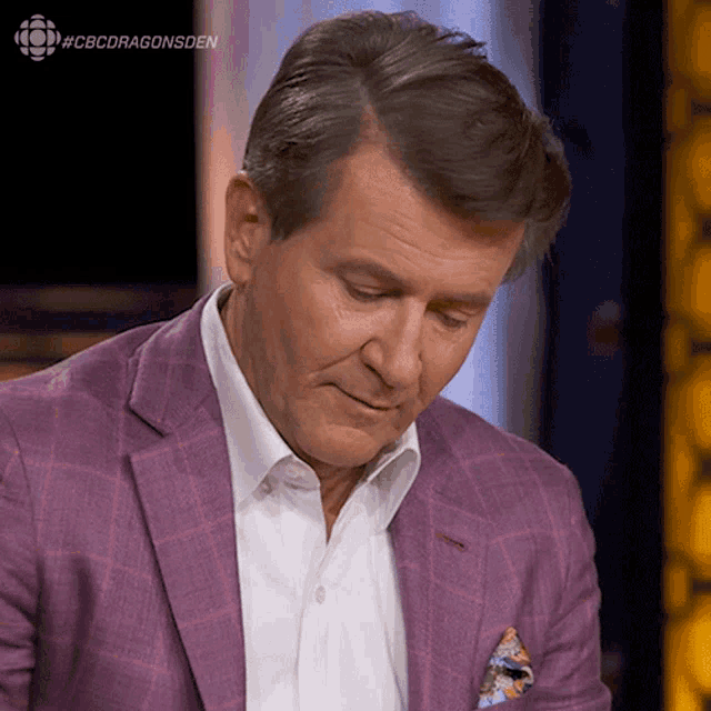 a man in a purple suit and white shirt is sitting in front of a screen that says cbcdragonsden