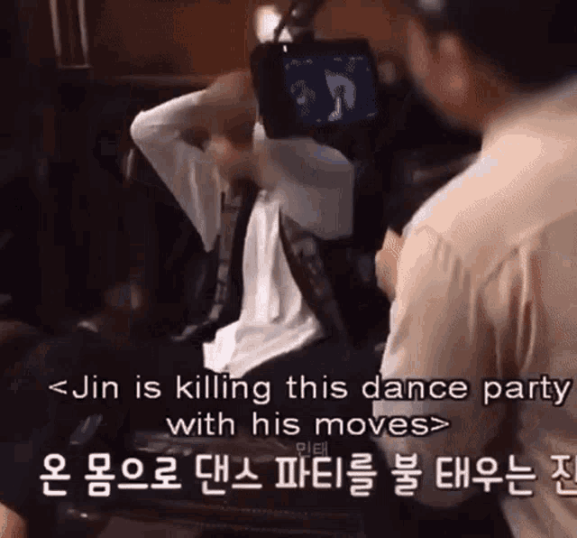 a man is sitting in front of a camera with the words jin is killing this dance party with his moves below him