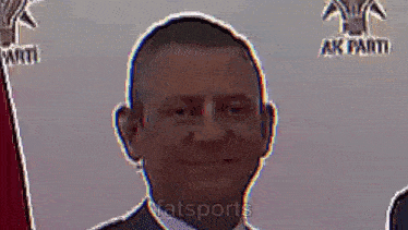 a man in a suit and tie is smiling in front of a flag and a sign that says ak parti .