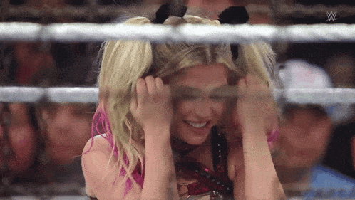a woman with pigtails is sitting in a wrestling ring and smiling .