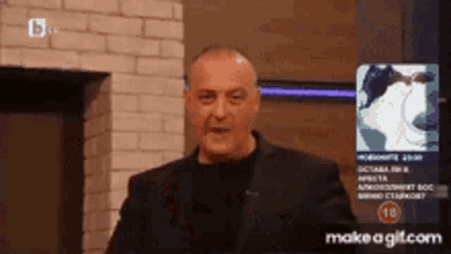 a man in a suit is standing in front of a screen that says make a gif.com on it .
