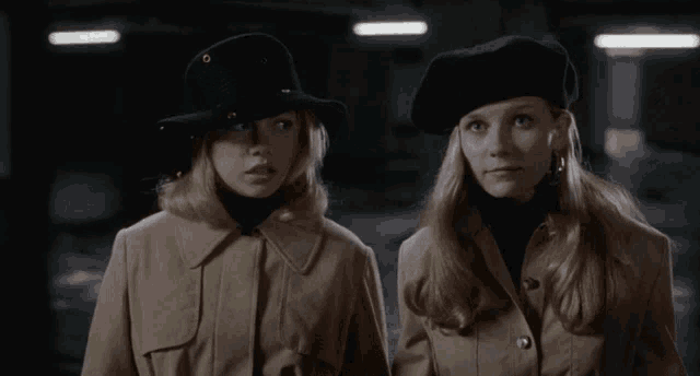 two women standing next to each other wearing hats