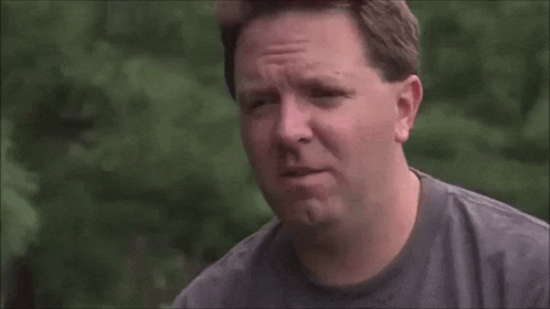 a man in a gray shirt is making a funny face while standing outside .