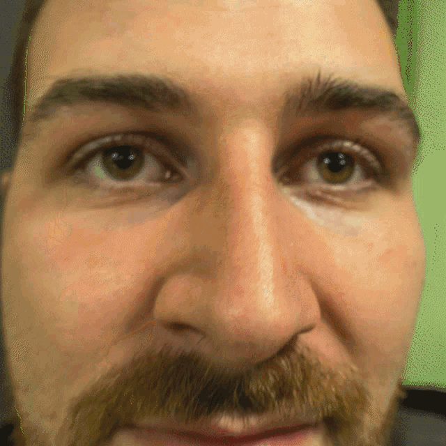 a close up of a man 's face with a beard and green eyes
