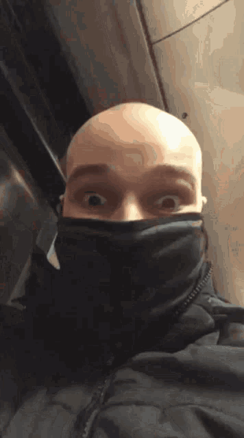 a bald man wearing a black mask looks surprised
