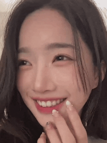 a close up of a woman 's face smiling with her hand on her chin .