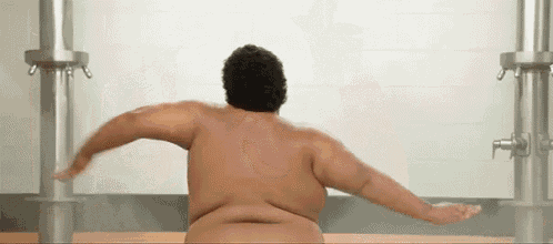 a naked man is standing in a shower with his arms outstretched and his back to the camera .