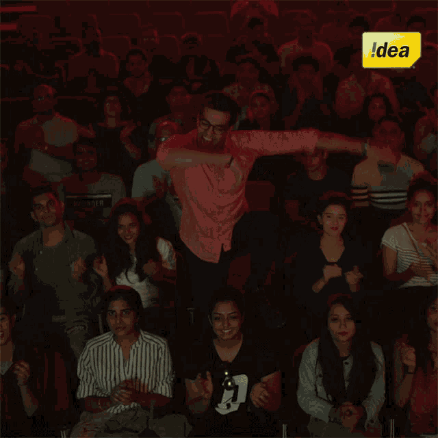 a man in a pink shirt is standing in front of a crowd of people with a yellow sign that says idea on it