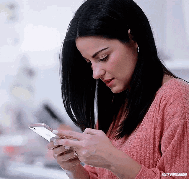 a woman in a pink sweater is using a smart phone