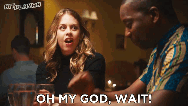 a man and a woman are sitting at a table with the woman saying oh my god wait