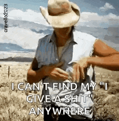 a man in a cowboy hat is standing in a field with a gun in his pocket .