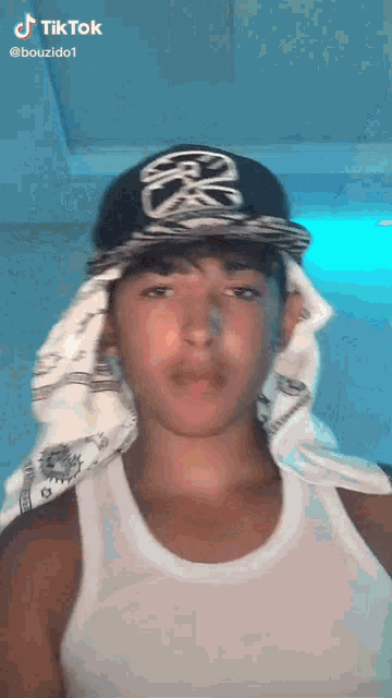 a young man wearing a white tank top and a hat with a skull on it