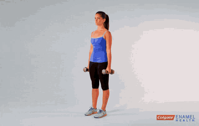 a woman in a blue tank top is holding dumbbells over her shoulder