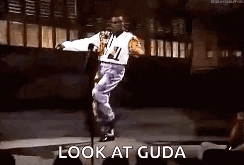 a man is standing on a pole on a stage with the words `` look at guda '' written next to him .