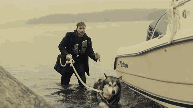 a man pulls a dog out of the water next to a triton boat