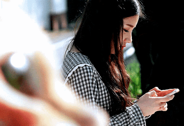 a woman in a plaid shirt looks at her cell phone