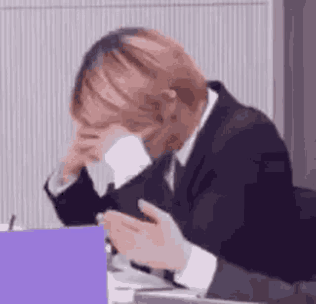 a man in a suit and tie is sitting at a desk holding a cell phone in his hand .