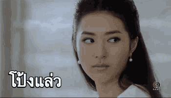a woman in a white shirt and pearl earrings is looking at the camera with a serious look on her face .