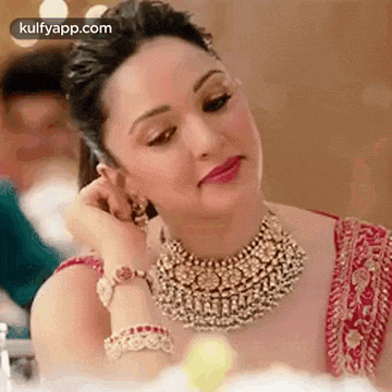 a woman wearing a necklace and earrings is sitting at a table and adjusting her earring .