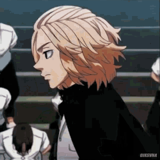 a man with long blonde hair is standing in front of a group of people in a classroom .