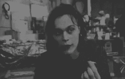 a woman is smoking a cigarette in a room in a black and white photo .