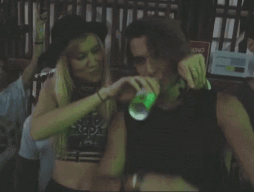 a man and a woman are drinking from a green bottle in a dark room