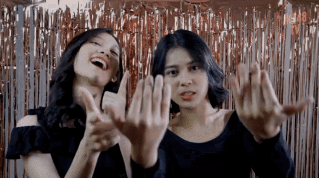 two girls are making funny faces in front of a tinsel curtain