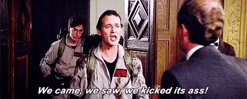 a man in a ghostbusters uniform is talking to a man in a suit while another man looks on .