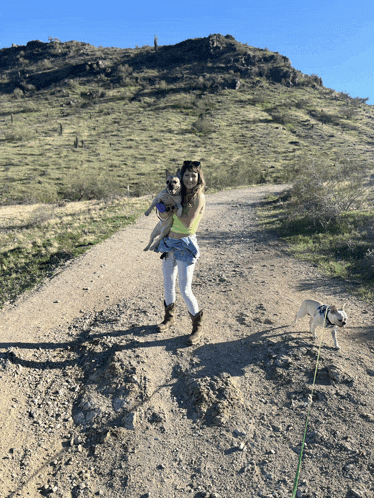 a woman holds two dogs on a dirt road