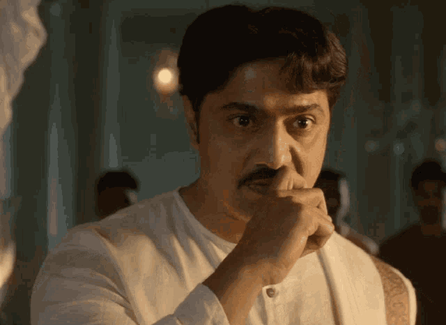a man with a mustache and a white shirt is covering his mouth with his hand