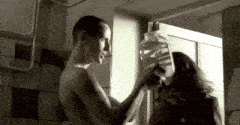 a man and a woman are standing next to each other in a bathroom . the man is holding a jar of water .