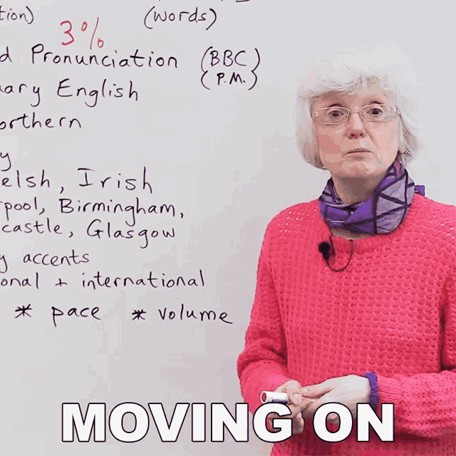 a woman in a pink sweater stands in front of a whiteboard that says moving on on it