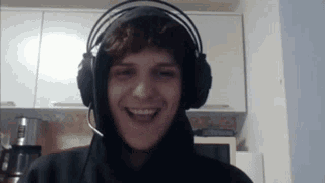 a young man wearing headphones and a microphone smiles at the camera