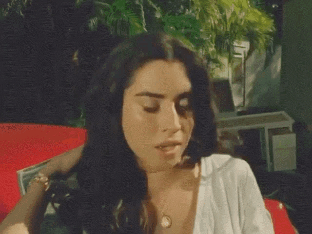 a woman with long dark hair is sitting on a red couch and looking at the camera .