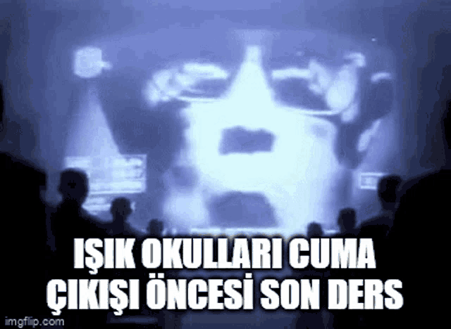 a group of people are sitting in front of a projector screen with a picture of a man 's face on it .