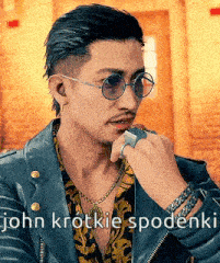 a man wearing a leather jacket , sunglasses , a ring and a necklace .