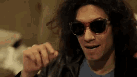 a man with curly hair wearing sunglasses and a leather jacket is smiling .