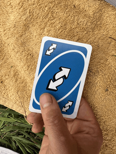a hand is holding a blue uno card with arrows pointing in opposite directions