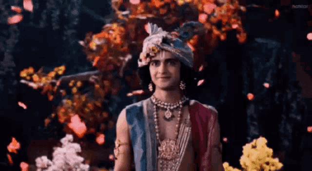 a man in a turban is standing in front of a tree surrounded by flowers and petals .