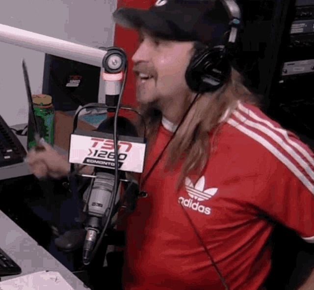 a man wearing headphones and a red adidas shirt is talking into a microphone