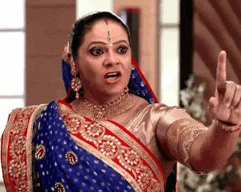 a woman in a blue and red saree is pointing her finger at something