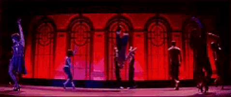 a group of people are dancing on a stage with red lights behind them