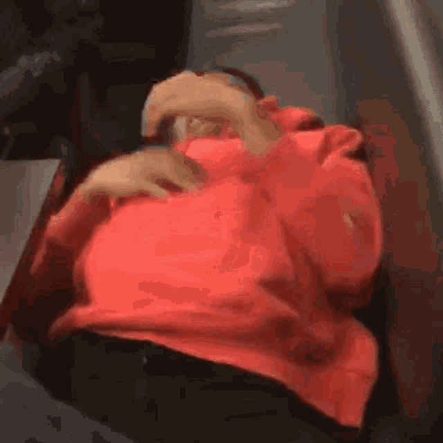 a man in a red sweatshirt is sleeping on a couch with his hand on his chest .