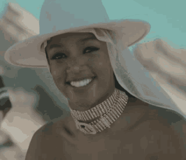 a woman wearing a pink hat and a choker is smiling and looking at the camera .