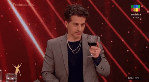 a man in a suit holds a glass of wine in front of a screen that says america vivo