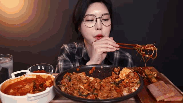 a woman with glasses is eating noodles with chopsticks